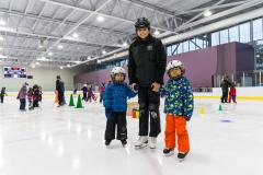 Skating instructor holding hands with two children on indoor ice