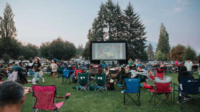 Giant movie screen at the park with lots of attendees watching from lawn chairs